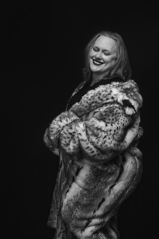 Woman smiling softly in a luxurious fur coat, radiating warmth and quiet glamour in a studio portrait.