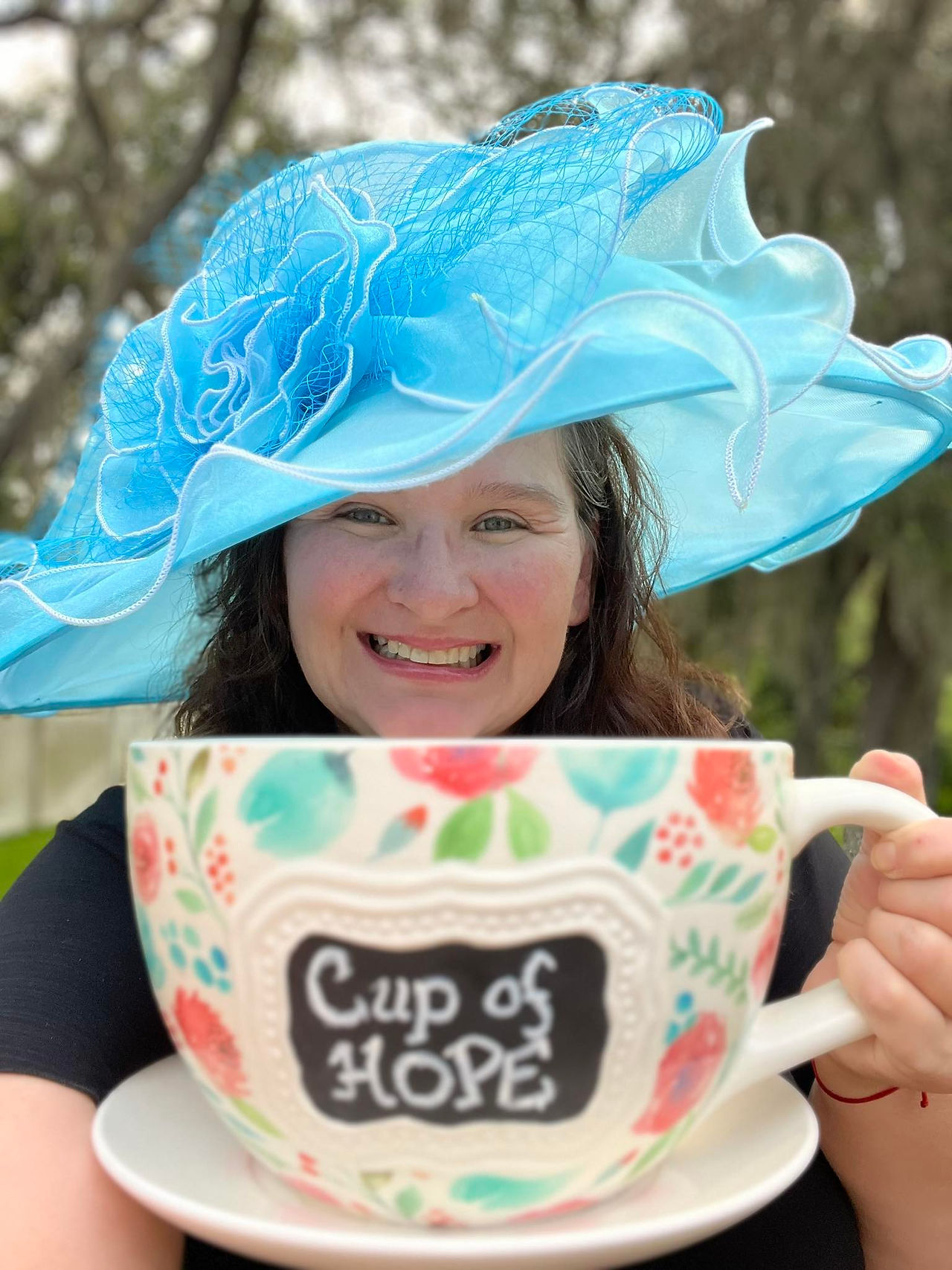 Woman in a blue hat holding a large teacup that says “Cup of Hope”