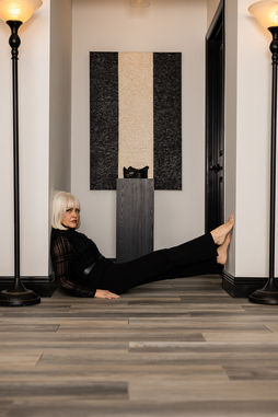 GiGi leaning back on her hands with her legs extended beneath a geometric painting.