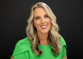 Studio headshot of a healthcare provider in a green dress against a dark background.