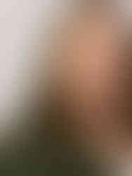 Brightly lit self-portrait of a woman in a green jacket, smiling with a warm and friendly expression, white backdrop.