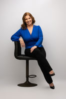 Studio personal branding portrait of a businesswoman in a blue blazer seated on a stool.
