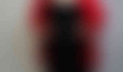 Full-body portrait of a confident woman wearing a bold red blazer, black dress, and matching red heels, standing with hands on hips and smiling in a studio setting.