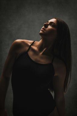 Moody low light portrait of a woman in a black bodysuit looking upward, beauty photography in Central Florida.