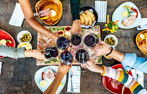 Friends cheering red wine glasses on table covered with delicious food at at farm house vi