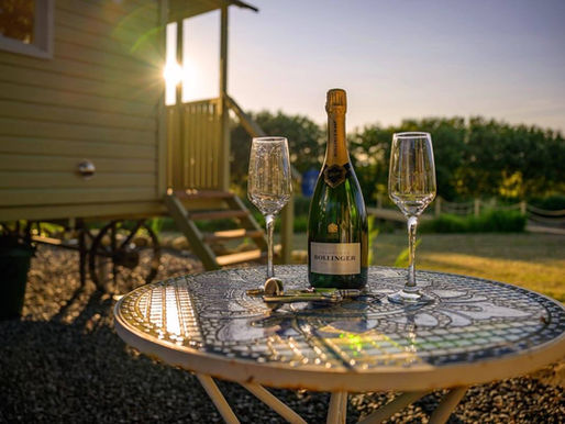 A bottle of champagne and two glasses on a table outside one of the huts at Brook Cottage Shepherd Huts
