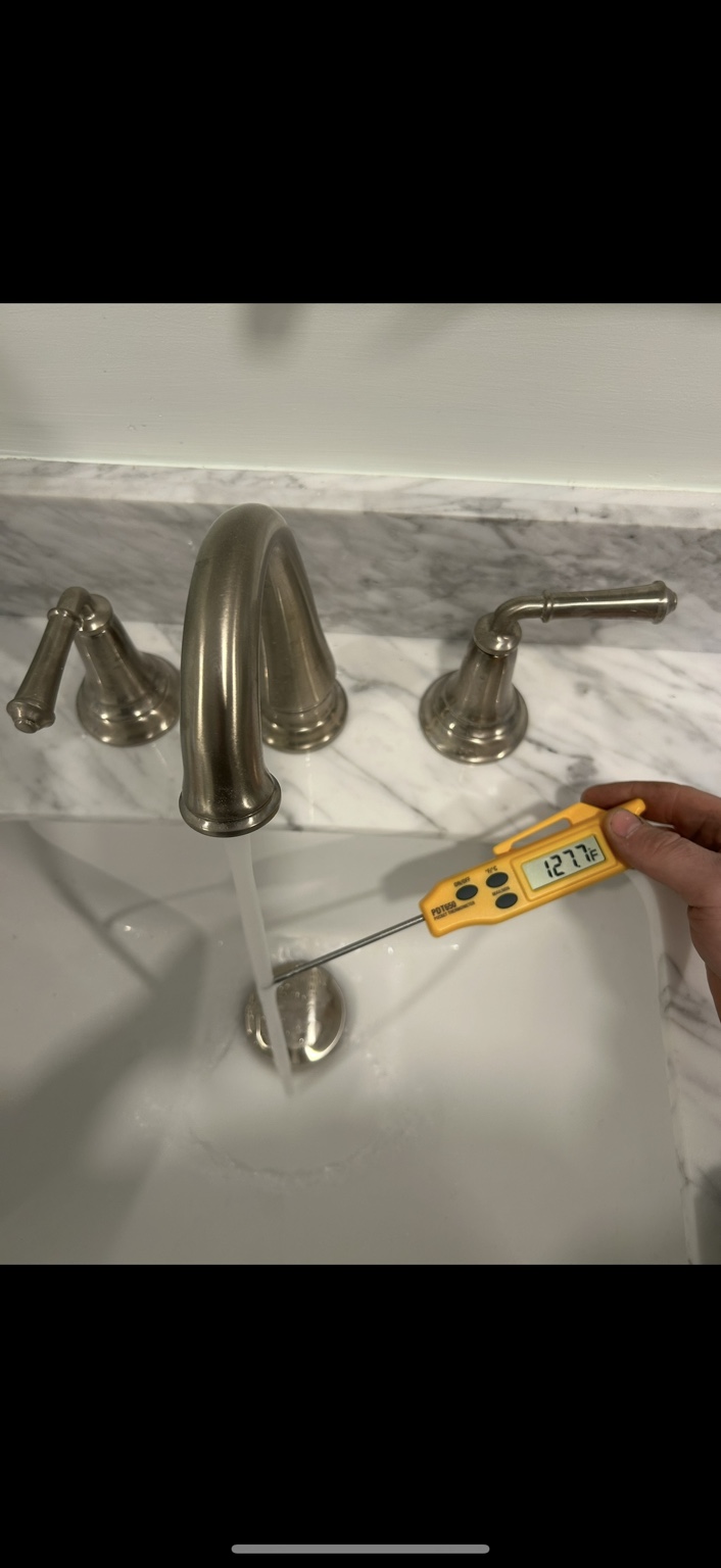 Technician using a digital thermometer to check running water at a bathroom faucet