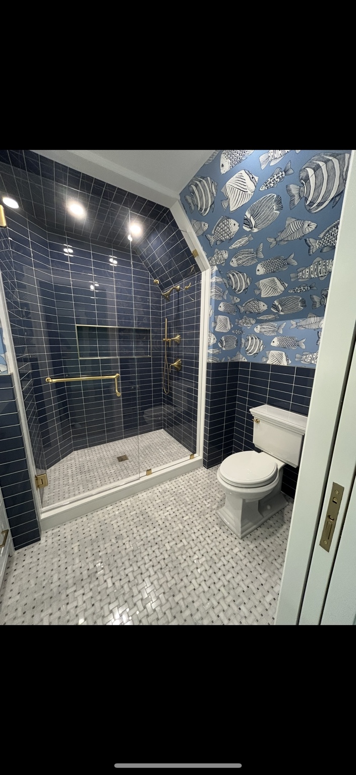 Blue tiled shower with brass shower fixtures and a white toilet