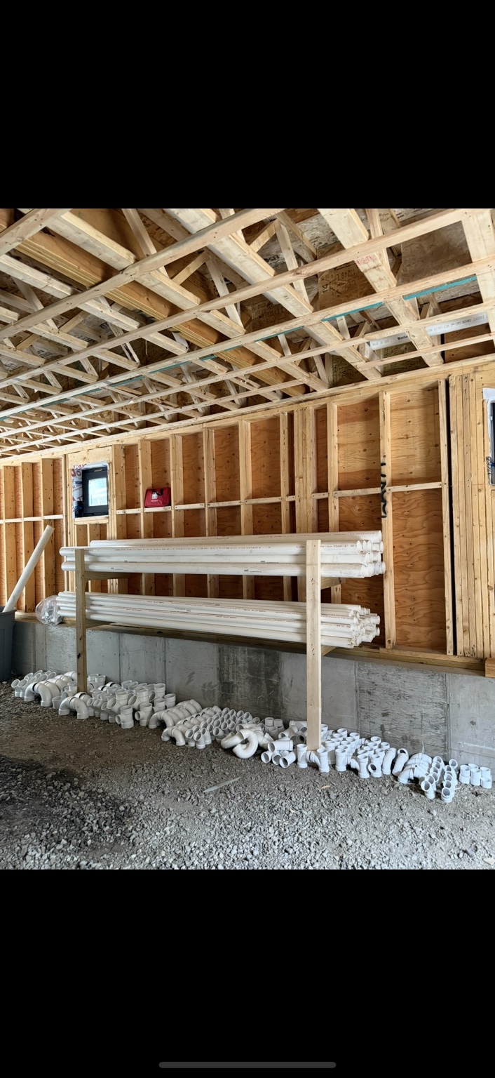 Drainage pipe and fittings organized beside exposed framing before installation