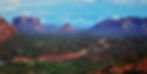 Red rocky mountains and green forest landscape in Sedona under a blue sky with white clouds. Serene and expansive mood.