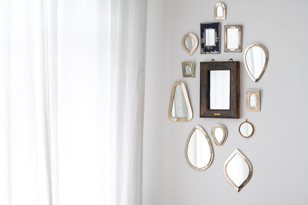 A collection of circular, oval, and rectangular mirrors in varying sizes displayed together on a wall. The mirrors have frames made of both metal and wood materials. The metal frames are thin, metallic, and silver or gold in color. The wood frames are wider, with a natural brown stained finish. The different shaped mirrors are clustered together in an alternating layout, creating visual interest on the wall.