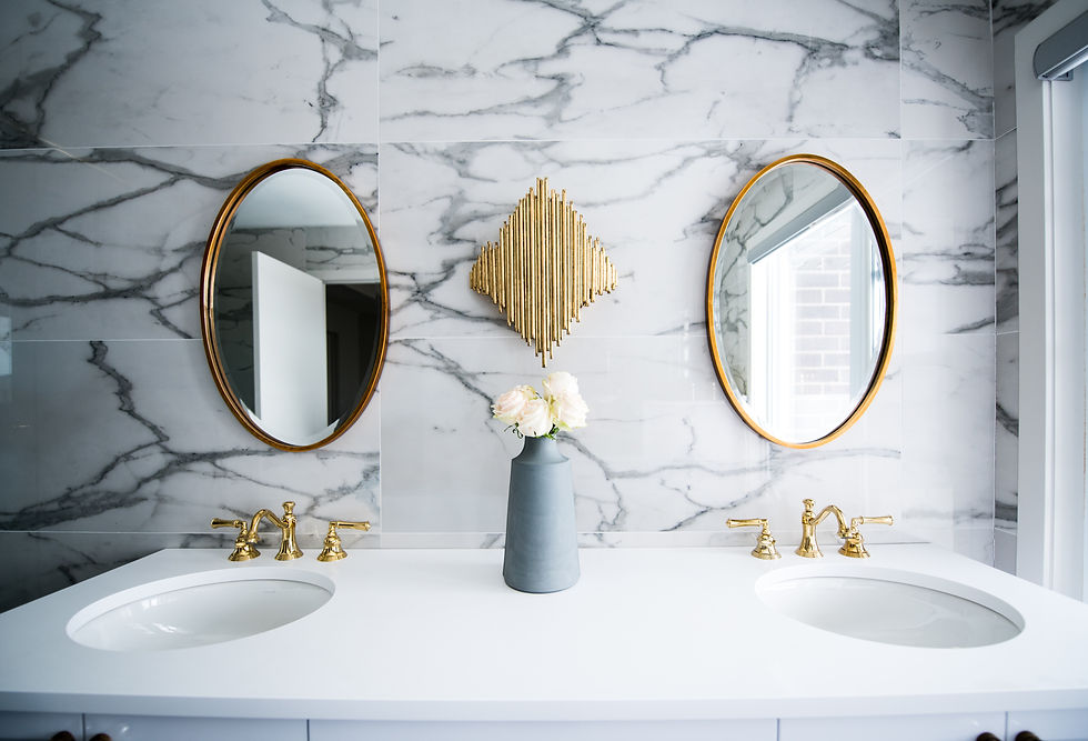 Pair of oval-shaped bathroom mirrors with gold metal frames hanging vertically on a wall above two separate sinks. The mirrors have a polished, reflective surface and elegant curved frames.