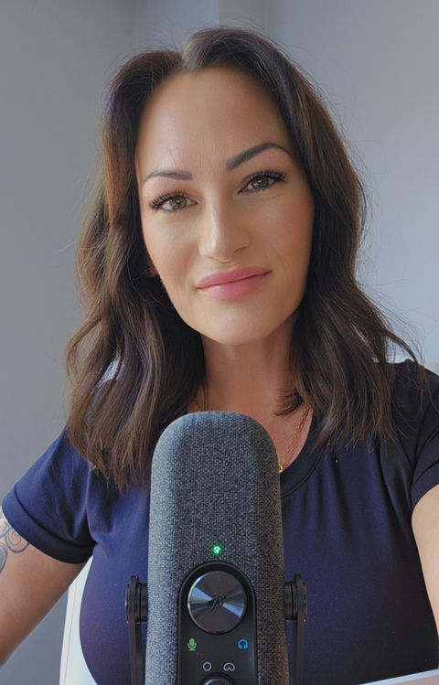 Woman speaking into a large microphone in a bright home studio, with a calm expression and gray wall behind her. Stephanie Gelinas.