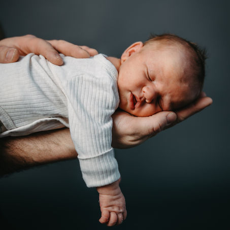 Sovende baby på magen med mørkeblå bakgrunn og pappas hender som omfavner han trygt