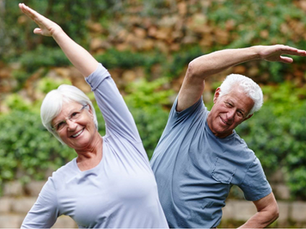 Smiling elderly couple stretching outdoors in a green garden, arms raised overhead