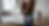 Elderly person in a brown cardigan holds their knee, standing near a beige sofa. The room is bright with light wood flooring. Mood: discomfort.