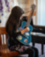 Child playing a blue acoustic guitar with colorful stickers