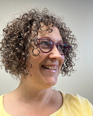 Norgyun (Elke) Kriegel, Registered Massage Therapist, close-up portrait in her treatment room with a white wall behind her, wearing glasses and smiling.