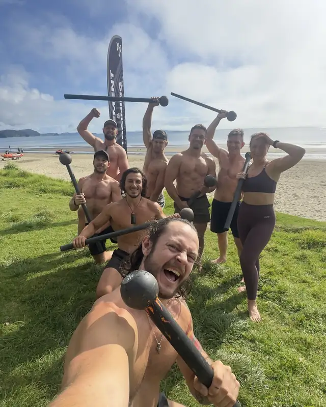The Kairos Saturday crew with their macebells on the grass at Ōrewa Beach, the Kairos flag behind them