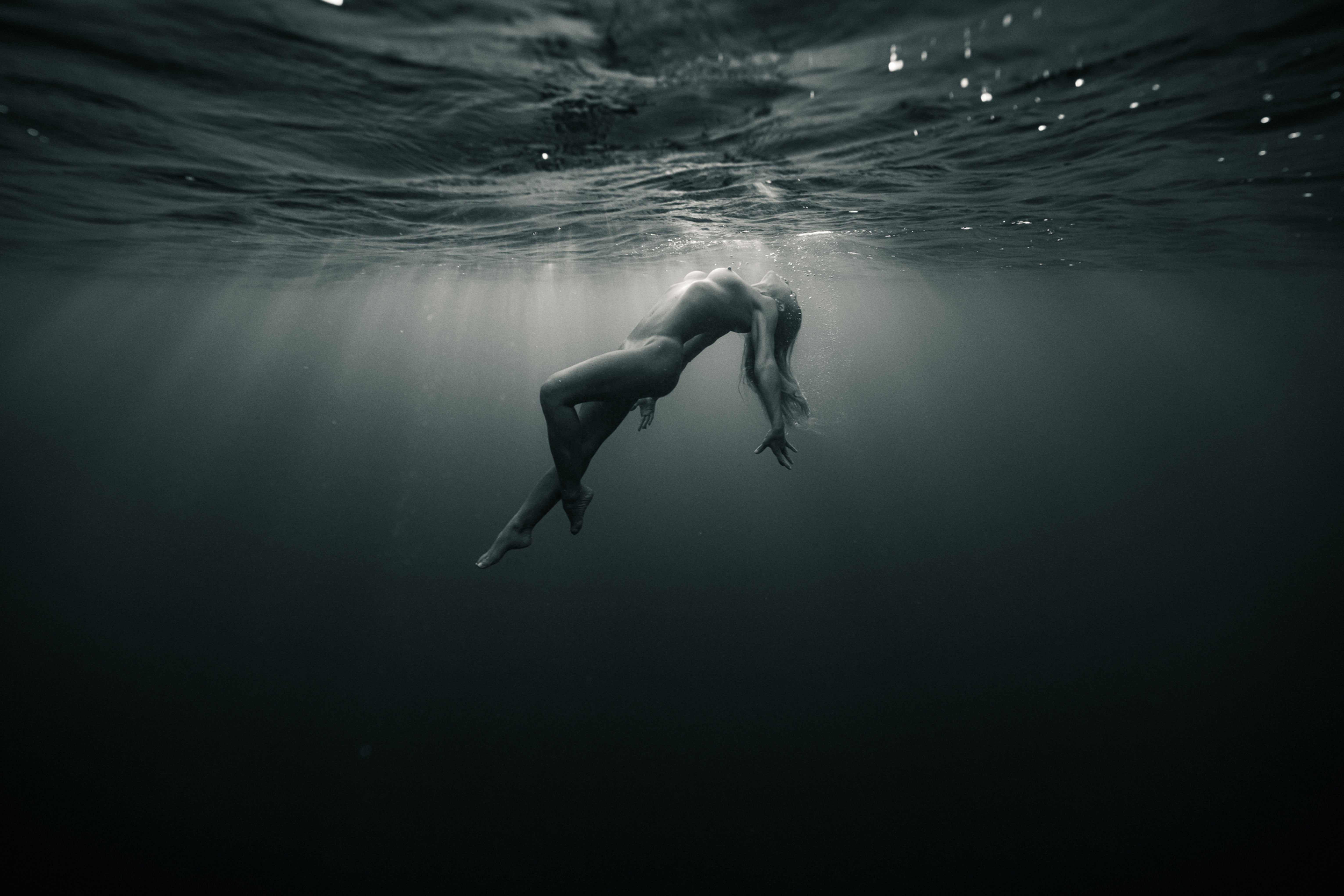 side view of a woman floating underwater with light breaking through the surface of the water