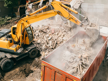 Excavator breaks building and loads construction waste into truck with its bucket.
