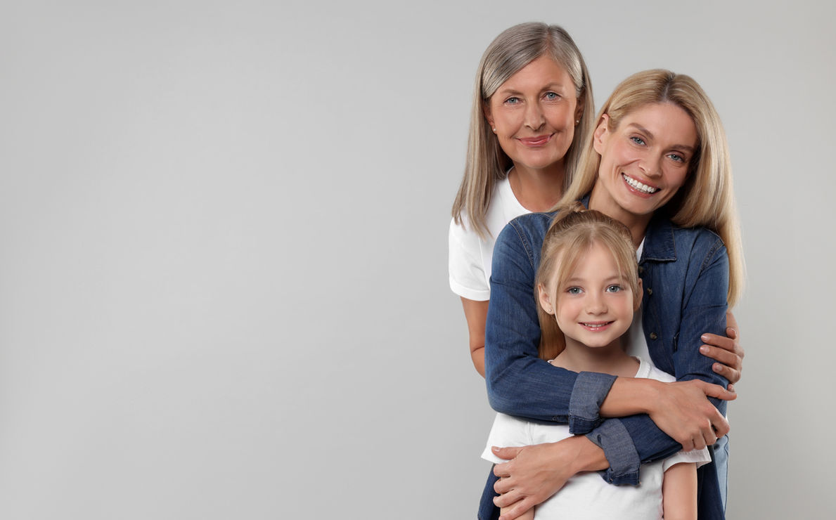 Three generations of women, all smiling on grey background