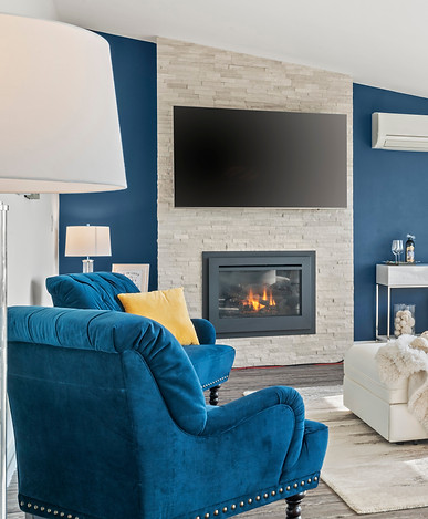 Welcoming living room with a blue accent wall, white faux fur pillows and a modern firepla