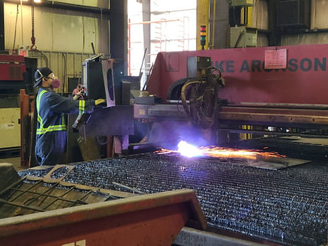 Worker operating a plasma cutter on structural steel.