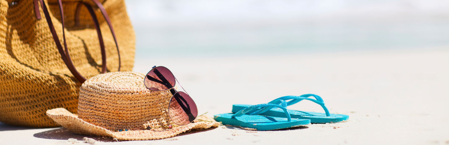 beach bag, hat, sunglasses, and blue flip flops on the beach