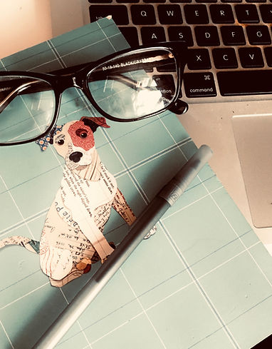 Photo of a journal with a dog on the cover. Sitting on top of the journal are glasses and a pan. The journal is next to a macbook keyboard