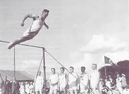 Das Bild, eine schwarz-weiß Fotografie, zeigt eindrucksvoll, wie ein Turner einen Salto, als Abgang, vom Reck macht.
