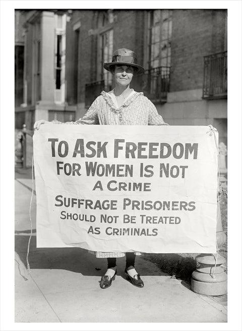 Woman holds a protest banner reading "To ask freedom for women is not a crime..." on a city street. She appears determined and serious.