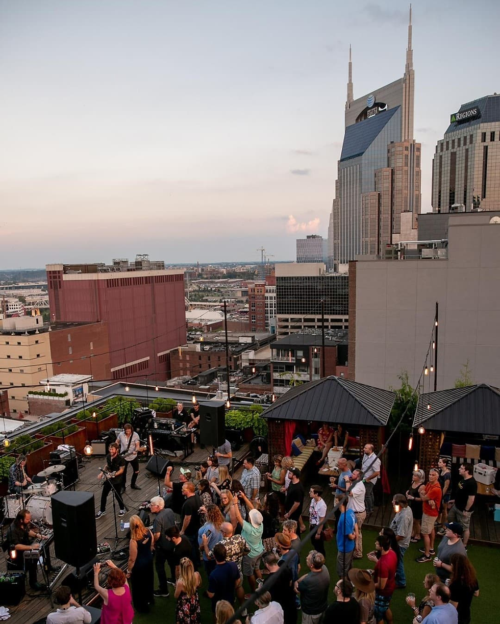 Crowd watches a rooftop live band at dusk, with Nashville skyline and AT&T and Regions towers behind.