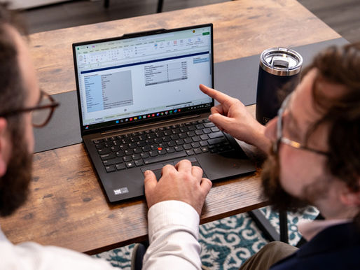 Two real estate professionals analyze a construction budgeting spreadsheet on a laptop, reviewing cost projections, contingency reserves, and underwriting assumptions for a development project in uncertain market conditions.