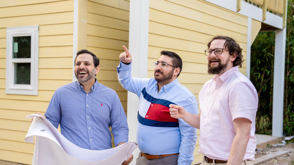 Three BETTER team members review plans and point toward a feature of a newly constructed yellow home.