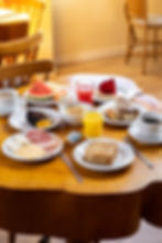 Mesa de café da manhã com opções de fruta, sucos, danones, pães e bolos na Pousada Kaliman em Campos do Jordão