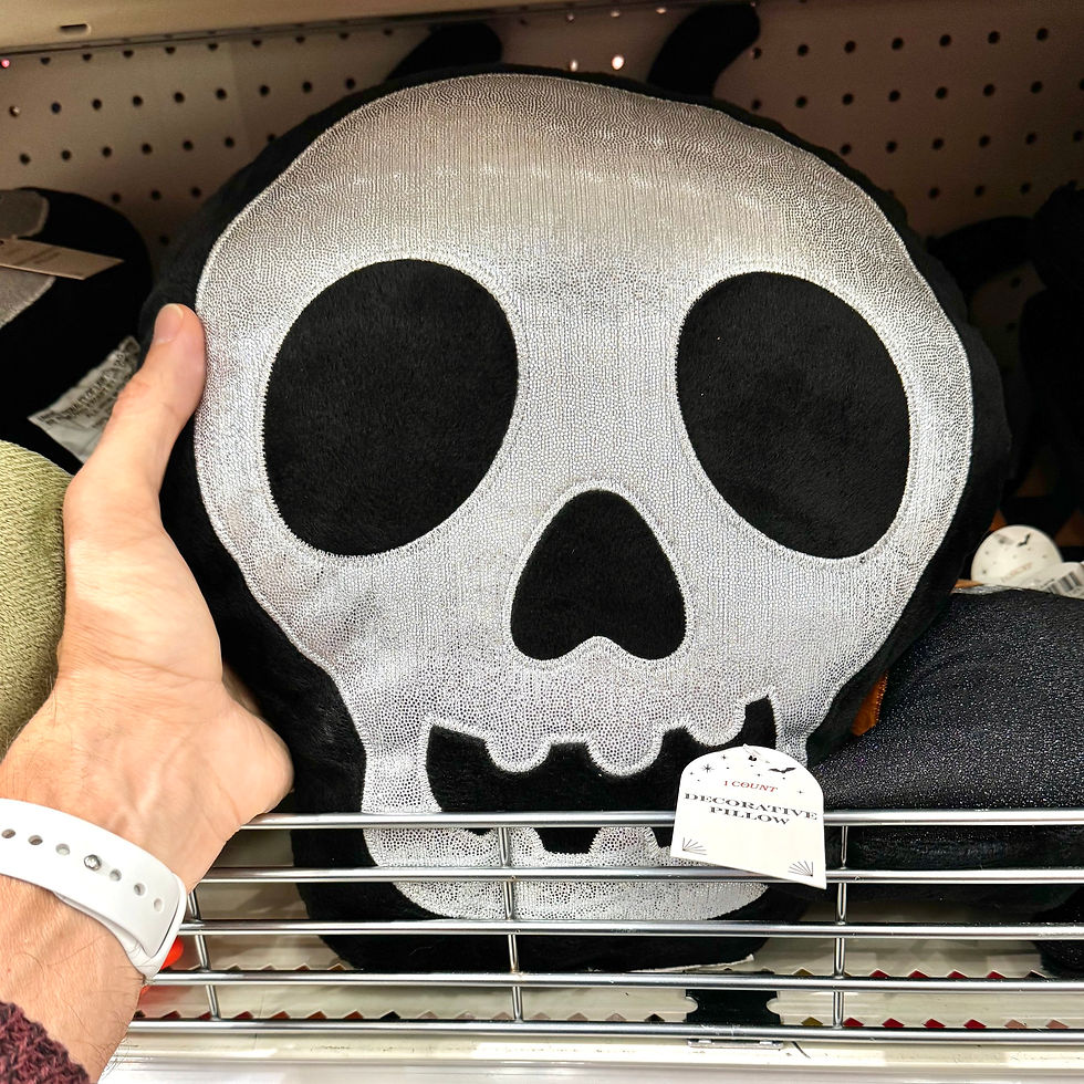 A hand holds up a black decorative pillow in the shape of a skull with a sparkly, silver design.