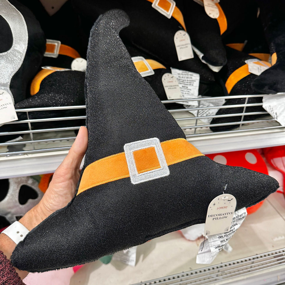 A hand holds a black witch hat-shaped pillow with a vibrant orange and silver buckle design.