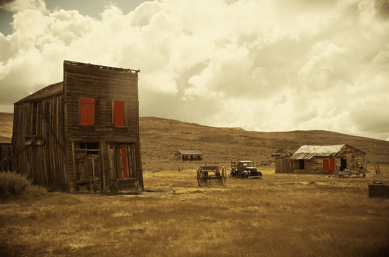 Photograph of Bodie, a desolate ghost town in the mountains of California. Eerie red glow in the windows of derelict wooden huts. Photo by Julien McRoberts.