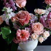 Moody rose arrangement in mauve, blush, and deep pink tones with textured greenery against a dark background