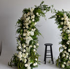White floral arch installation featuring clustered blooms and cascading greenery with a stool placed in the center