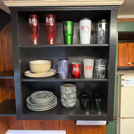 Cabinet with various cups and dishes. Different colors on the shelves.