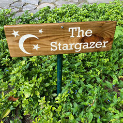 Wooden sign with stars and The Stargazer in front of green bushes.