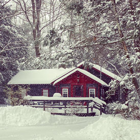 Snow covered cabin nestled among trees, winter scene Fireside Pines at Babbling Brook Cottages Poconos.