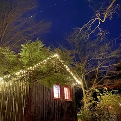 Wooden cabin with lights glowing at night with cozy vibes and nature.