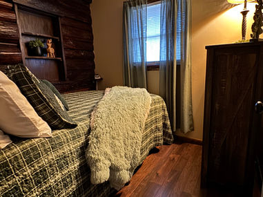 Cozy bedroom with bed, blanket, window, and wood paneling. Babbling Brook Cottages