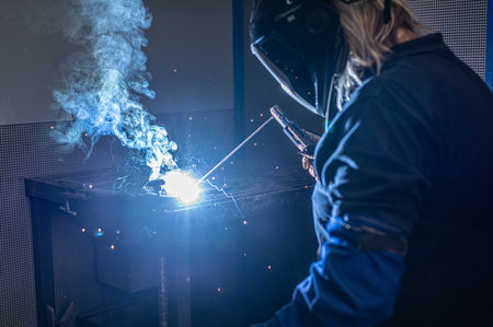 Person mit Schutzkleidung beim Schweißen – starke Licht- und Rauchentwicklung betonen die industrielle Tätigkeit.