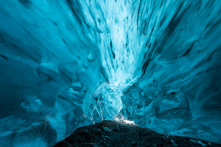 Tiefer Tunnel aus leuchtend blauem Eis mit schimmerndem Licht im Hintergrund.