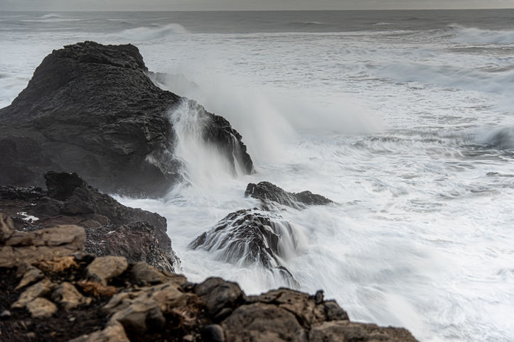 Dramatische Wellen brechen gegen schwarze Felsen an einer stürmischen Küste.