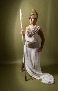 Frau im weißen Gewand steht mit einem Speer vor grünem Hintergrund.